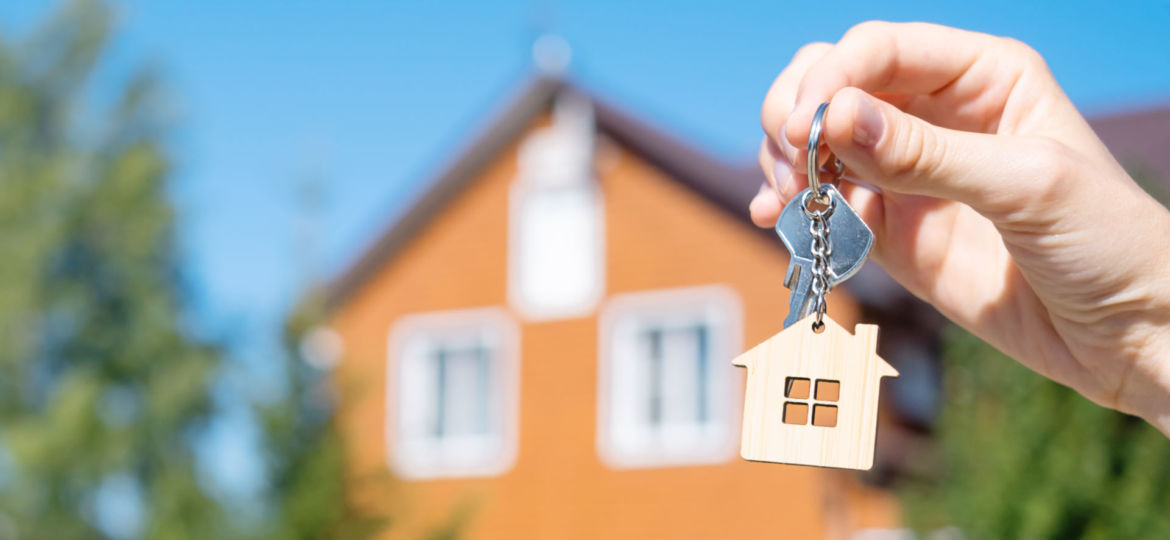 Close-up,Of,A,Key,With,A,House-shaped,Keychain,In,Hand.